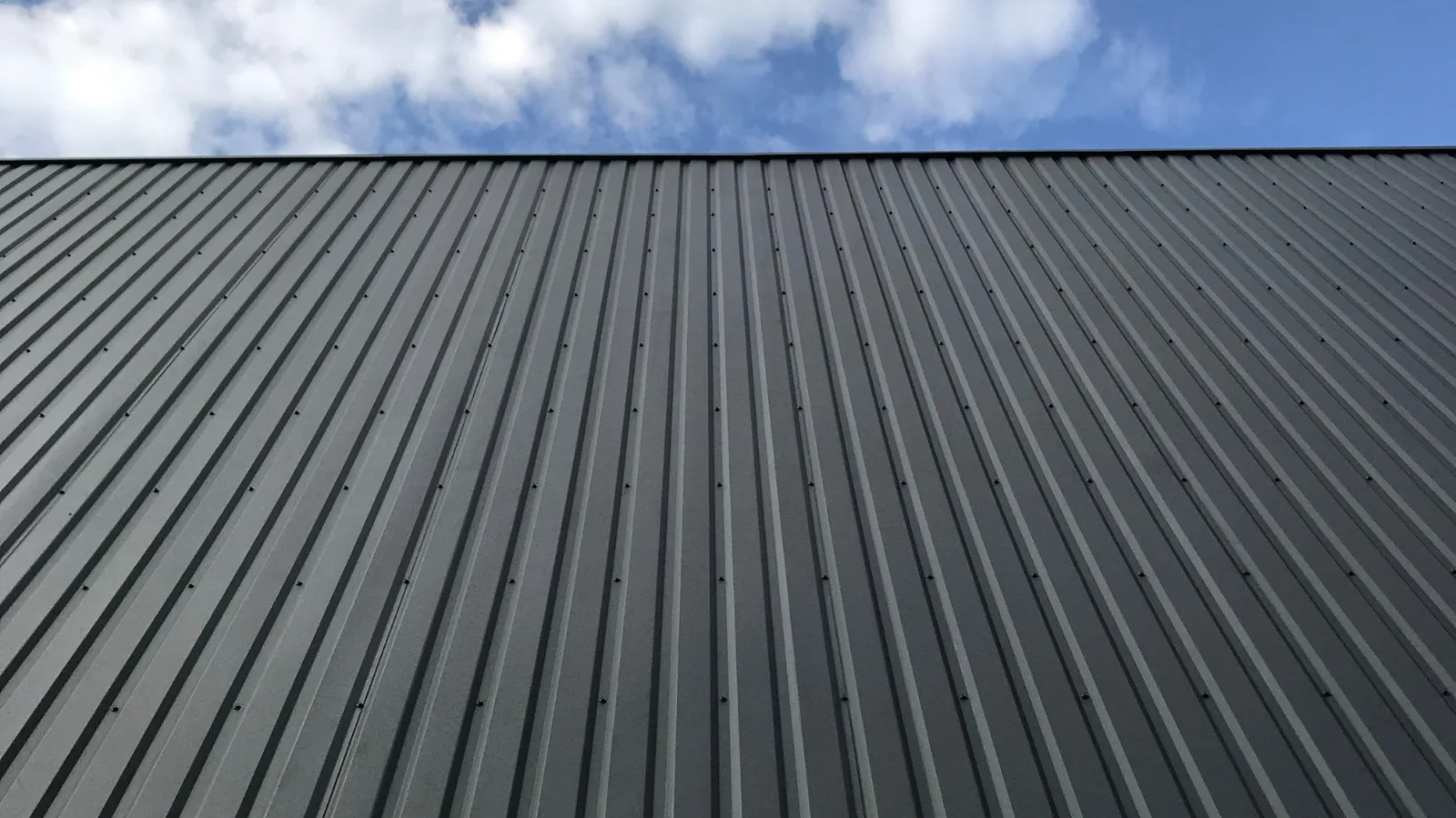 Dark ribbed metal panels rising toward a partly cloudy sky